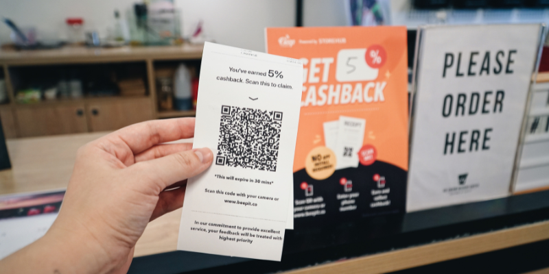 Hand holding receipt featuring a cashback QR Code